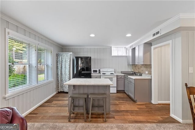 kitchen featuring gray cabinetry, a kitchen breakfast bar, hardwood / wood-style floors, and white appliances