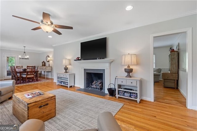 living room featuring light hardwood / wood-style flooring, ceiling fan with notable chandelier, and ornamental molding