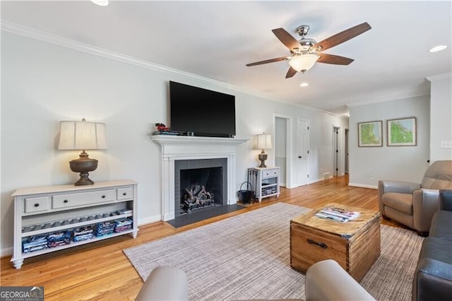 living room featuring light wood-type flooring, crown molding, ceiling fan, and a fireplace