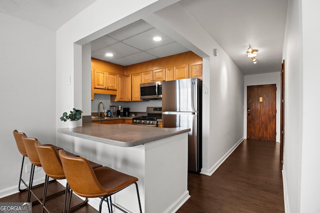 kitchen with a breakfast bar area, a peninsula, a sink, appliances with stainless steel finishes, and dark countertops