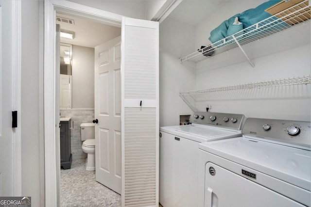 washroom with light tile patterned floors, washing machine and clothes dryer, and tile walls