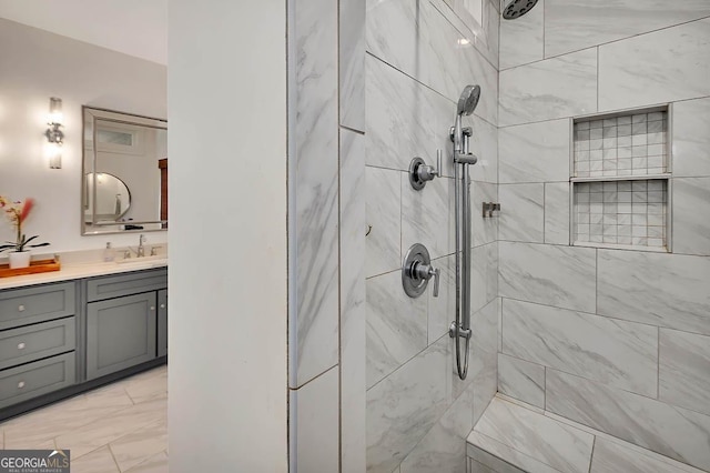 full bath featuring marble finish floor, tiled shower, and vanity