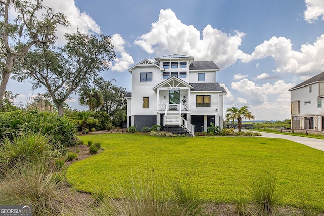 coastal inspired home featuring stairway, a front yard, and roof with shingles