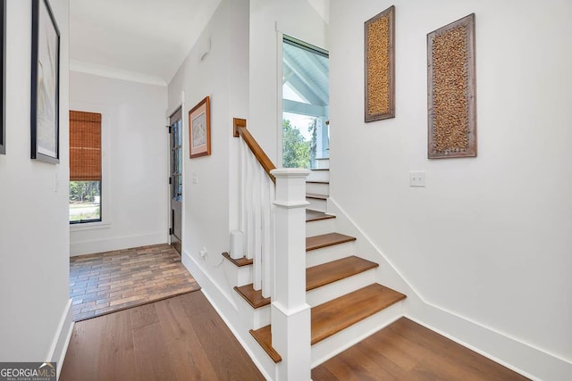 staircase with a healthy amount of sunlight, crown molding, baseboards, and wood finished floors