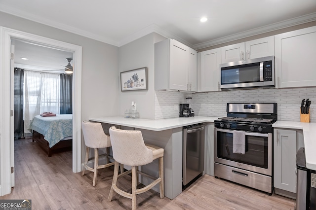 kitchen featuring ceiling fan, light hardwood / wood-style flooring, ornamental molding, a breakfast bar, and stainless steel appliances