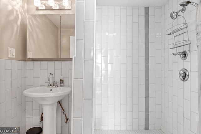 bathroom with tiled shower, a sink, and tile walls