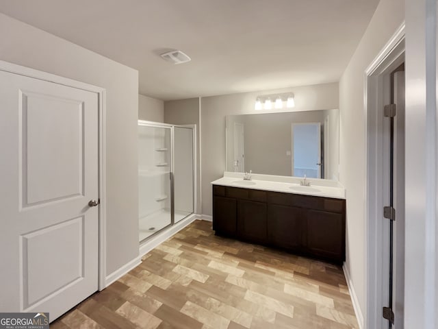 bathroom with wood-type flooring, a shower with shower door, and dual bowl vanity