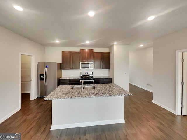 kitchen featuring a kitchen island with sink, light stone counters, appliances with stainless steel finishes, and dark hardwood / wood-style floors