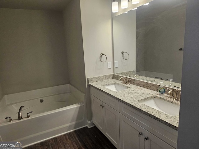 bathroom with double vanity, a garden tub, a sink, and wood finished floors