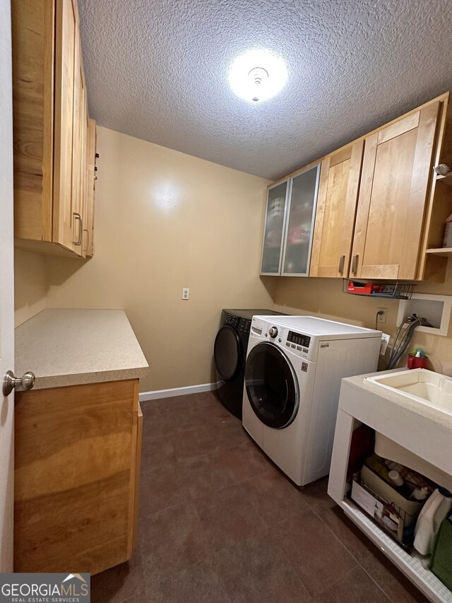 laundry area featuring a textured ceiling, washer and clothes dryer, and cabinets