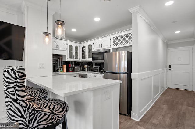 kitchen featuring white cabinets, a breakfast bar area, appliances with stainless steel finishes, glass insert cabinets, and a peninsula