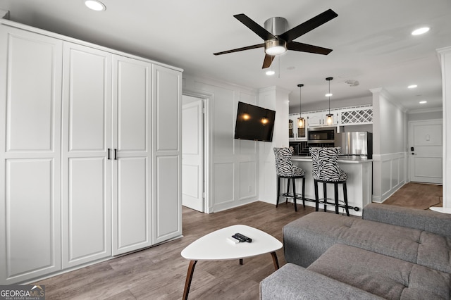 living area with ceiling fan, ornamental molding, wood finished floors, a decorative wall, and recessed lighting