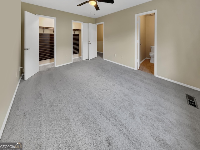 unfurnished bedroom with light carpet, baseboards, visible vents, ensuite bath, and a walk in closet