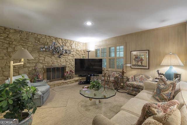 carpeted living room with a fireplace and wooden walls