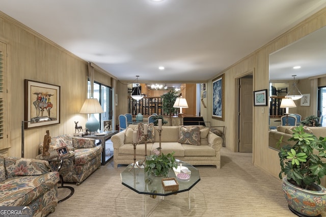 living room featuring wood walls, crown molding, an inviting chandelier, and light colored carpet