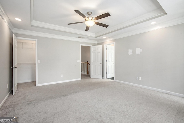 unfurnished bedroom with ceiling fan, a raised ceiling, light carpet, and a walk in closet