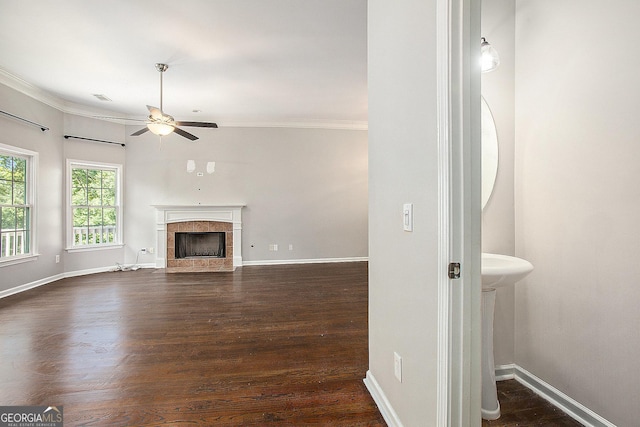 unfurnished living room with ceiling fan, a tiled fireplace, dark wood-type flooring, and crown molding