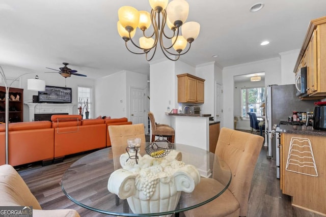 dining space with dark wood-type flooring, ceiling fan with notable chandelier, and crown molding