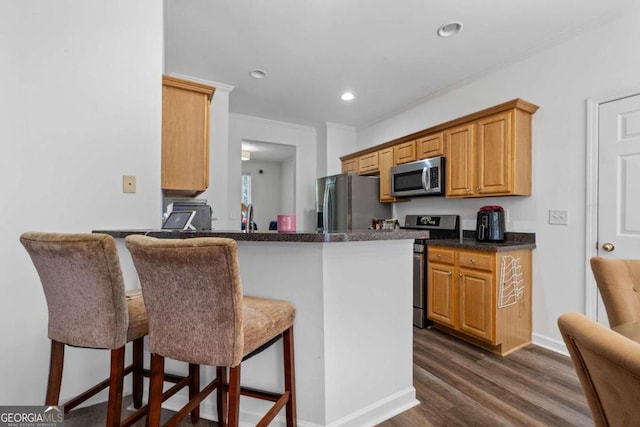 kitchen featuring appliances with stainless steel finishes, kitchen peninsula, dark hardwood / wood-style floors, and a kitchen bar