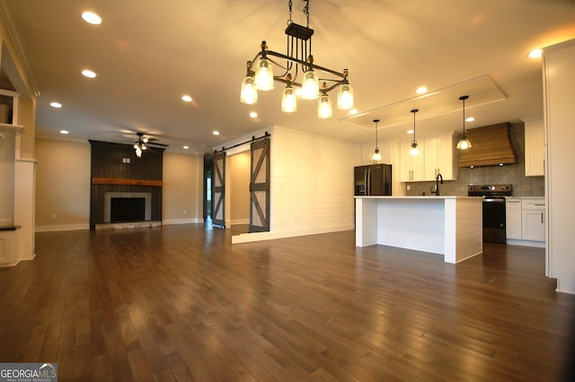 kitchen featuring stainless steel range with electric stovetop, custom range hood, a barn door, a kitchen island with sink, and white cabinets