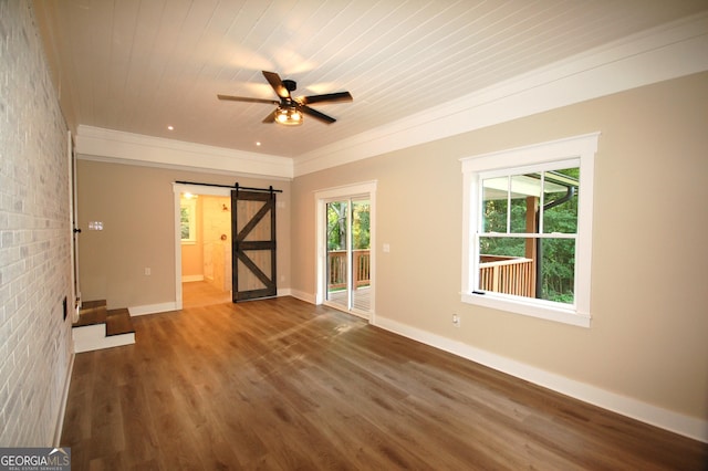 empty room featuring brick wall, a barn door, plenty of natural light, and dark hardwood / wood-style flooring