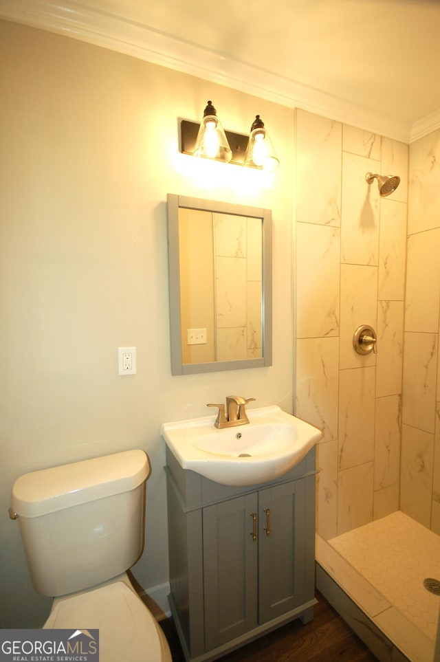 bathroom featuring a tile shower, vanity, ornamental molding, and toilet