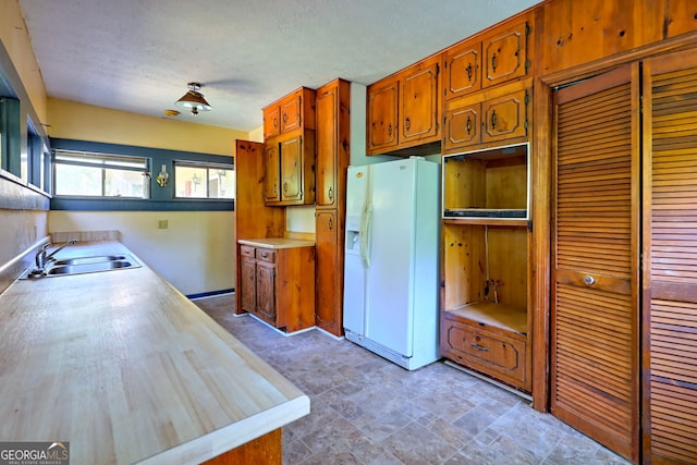 kitchen featuring white fridge with ice dispenser, a textured ceiling, sink, and tile patterned floors