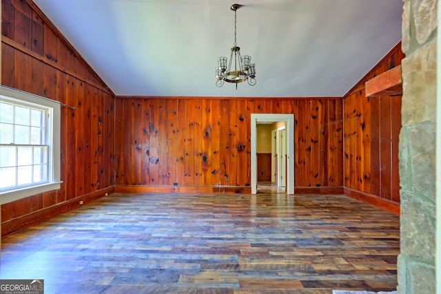 spare room featuring a chandelier, lofted ceiling, wooden walls, and wood finished floors