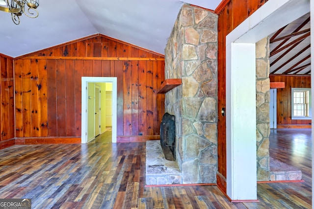 unfurnished living room with vaulted ceiling, a stone fireplace, wood-type flooring, and wooden walls