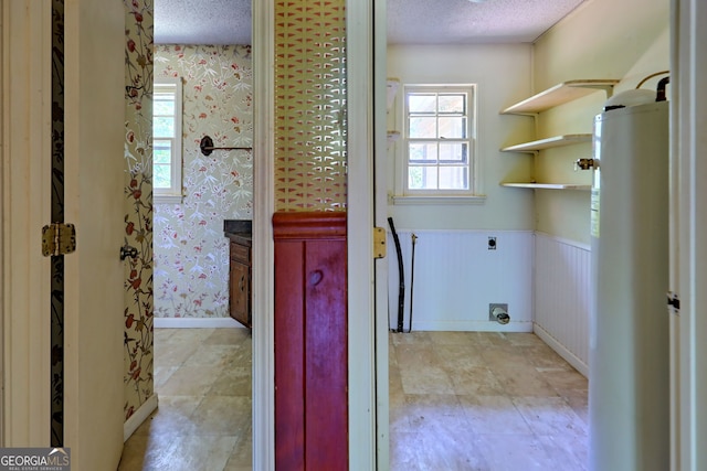 interior space featuring a textured ceiling, hookup for an electric dryer, wainscoting, and wallpapered walls