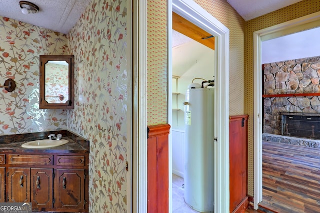 bathroom with hardwood / wood-style floors, a fireplace, gas water heater, a textured ceiling, and vanity