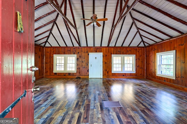 unfurnished living room with vaulted ceiling with beams, wooden walls, hardwood / wood-style floors, and ceiling fan