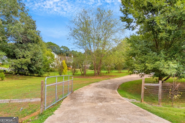 view of property's community featuring a yard, concrete driveway, and a gate