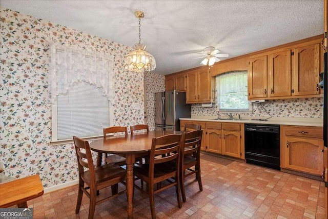 kitchen with sink, ceiling fan with notable chandelier, dishwasher, stainless steel fridge, and pendant lighting