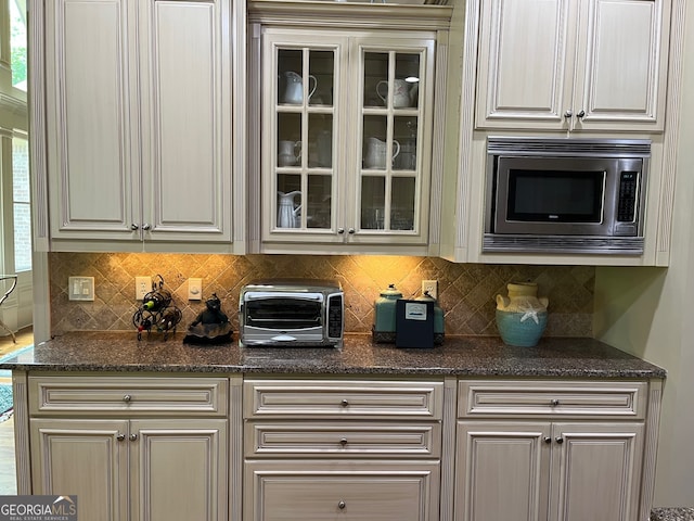 kitchen featuring backsplash, dark stone countertops, and stainless steel microwave