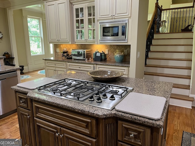 kitchen with decorative backsplash, dark brown cabinetry, light hardwood / wood-style floors, a center island, and stainless steel appliances