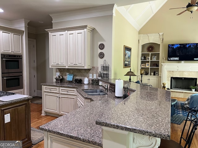 kitchen featuring decorative backsplash, hardwood / wood-style floors, sink, double wall oven, and a tiled fireplace