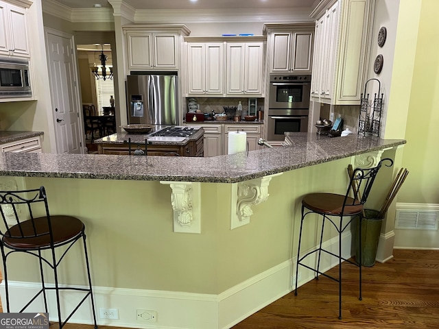 kitchen with kitchen peninsula, stainless steel appliances, dark hardwood / wood-style flooring, and dark stone counters