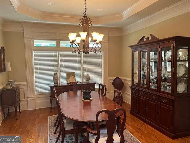 dining area featuring a raised ceiling, a notable chandelier, hardwood / wood-style floors, and ornamental molding