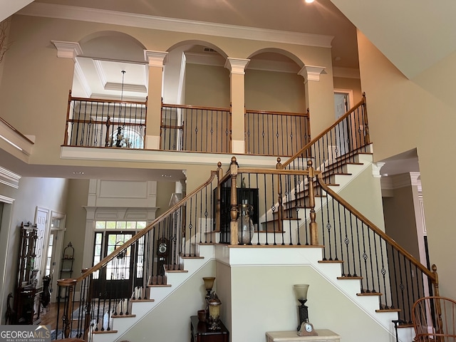 staircase with ornate columns, a towering ceiling, and crown molding