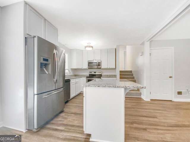 kitchen with light hardwood / wood-style flooring, a breakfast bar, white cabinetry, appliances with stainless steel finishes, and light stone counters