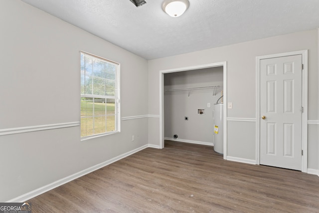 unfurnished bedroom with a textured ceiling, electric water heater, and hardwood / wood-style flooring