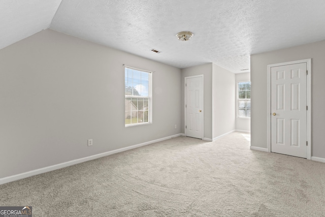 carpeted empty room with a textured ceiling and vaulted ceiling