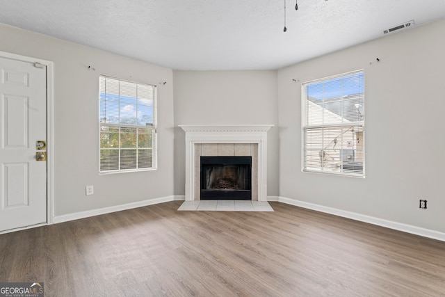 unfurnished living room featuring a textured ceiling, wood-type flooring, and a tiled fireplace