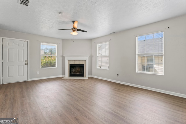 unfurnished living room featuring ceiling fan, a textured ceiling, hardwood / wood-style floors, and a tile fireplace