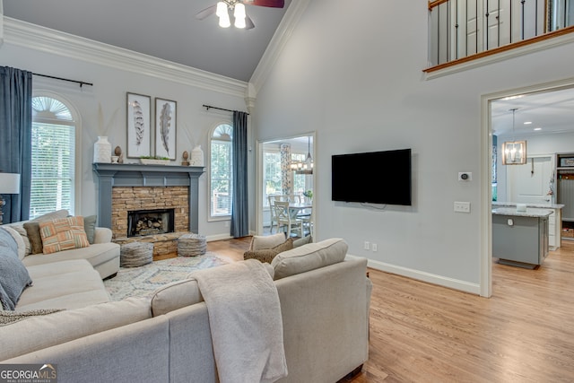 living room with light hardwood / wood-style floors, ceiling fan with notable chandelier, ornamental molding, and a fireplace