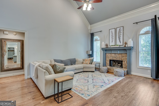 living room with vaulted ceiling, crown molding, light wood-type flooring, ceiling fan, and a stone fireplace