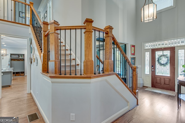 foyer entrance featuring hardwood / wood-style flooring, crown molding, a high ceiling, and a chandelier