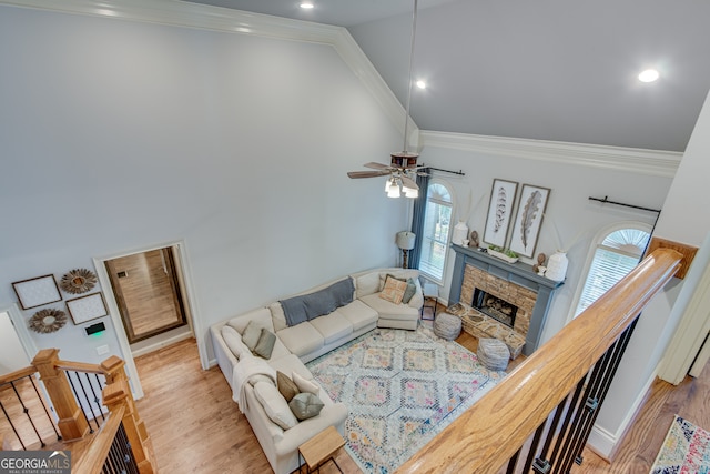 living room featuring a stone fireplace, ceiling fan, hardwood / wood-style floors, and ornamental molding