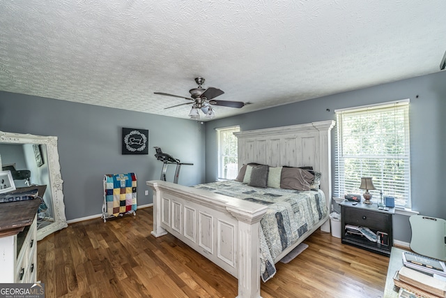 bedroom featuring a textured ceiling, ceiling fan, multiple windows, and hardwood / wood-style flooring